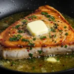 Pan-seared fish steak in a pan with butter, herbs, and spices