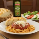 A plate of spaghetti with red sauce and Parmesan cheese, served with focaccia bread, a side salad, olive oil, and a glass of red wine.